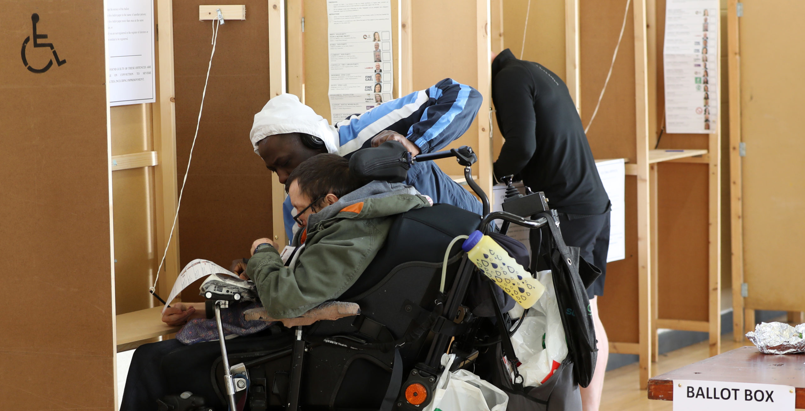 Image of person in wheelchair being assisted voting.